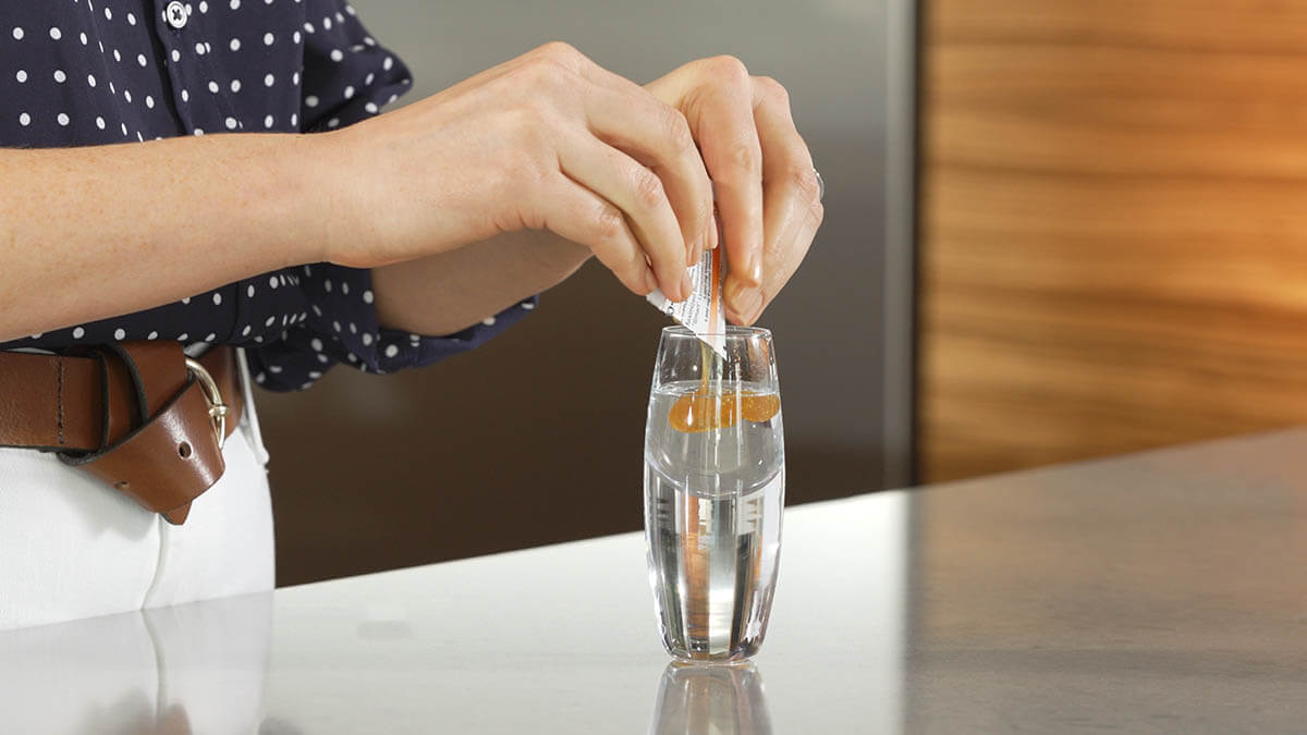 woman's hands squeezing a packet of liposomal vitamin c into a shot glass