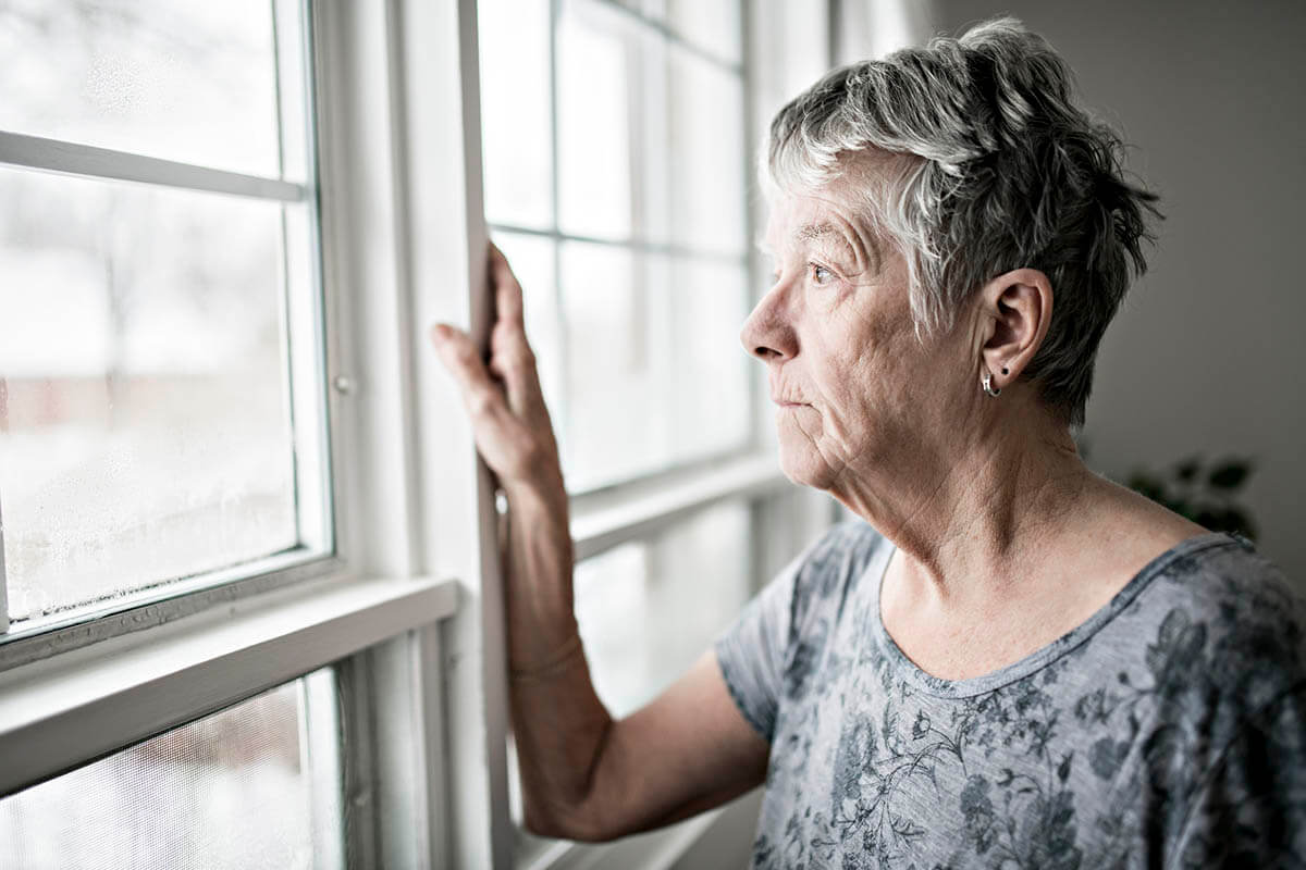 older woman in social isolation looks out the window
